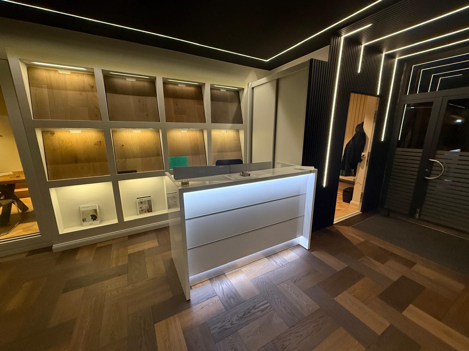 Accueil du showroom SP Construction avec parquet chêne en bâtons et niches d'échantillons éclairées